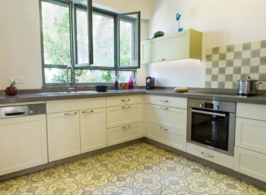 The gray and green hues of the kitchen floor, cabinets, tiles and countertop are in harmonie with the olive-green aluminum windows and with the green of the tiny garden outside.