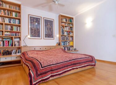 מדפי ספרים משני צידי המיטה. חלקם התחתון כולל מגירות, ומשמש כשידות משני צידי המיטה. מאחורי המיטה - ארגז מצעים.