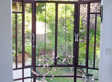 חלון אקווריום גדול מפרופיל בלגי ברזל מאפשר קשר בין הבית לגינה היפה שסביבו.