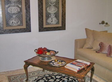 חדר הארוח הסמוך לסלון רוהט בבגוונים של קרם, עם שתי תמונות בעלות נוכחות מרשימה כמוקד החדר.