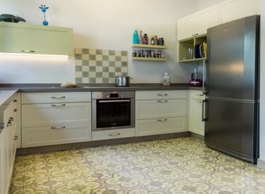 The gray and green hues of the kitchen floor, cabinets, tiles and countertop are in harmonie with the olive-green aluminum windows and with the green of the tiny garden outside.